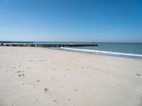 a beach with a pier over the water next to a sandy shore line and waves