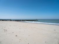 a beach with a pier over the water next to a sandy shore line and waves