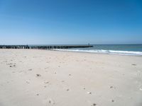 a beach with a pier over the water next to a sandy shore line and waves