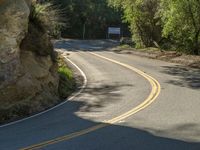 a person riding on the road with a large rock wall around them and trees all around them