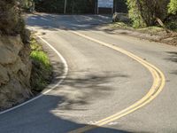 a person riding on the road with a large rock wall around them and trees all around them