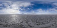 there are some clouds above a body of water with mountains in the background and snow covered ground