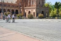 a group of people riding on top of bikes on a brick road in front of an old building