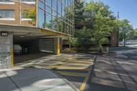 the building has multiple parking spaces underneath it, with no windows, with two doors opened to allow cars on the sidewalk