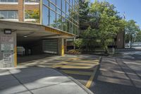 the building has multiple parking spaces underneath it, with no windows, with two doors opened to allow cars on the sidewalk