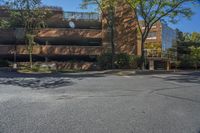 a parking lot next to a brown building on top of a street lined with trees