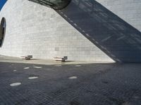 the shadow of the wall has made of bricks and cement on it and on to the bricks are benches