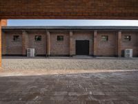 an empty courtyard has bricks on either side and a brick wall with a small square door in the middle