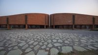 a walkway leads to two circular brick buildings with circular balconies on one side and small stones on the other