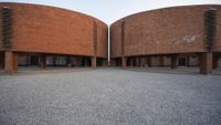 a walkway leads to two circular brick buildings with circular balconies on one side and small stones on the other