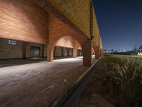 an empty brick walkway that leads into an alley that has an outdoor theater, and tall grass growing on the other side