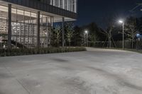 a large concrete slab in front of a glass building at night with lights on in the distance