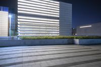 a concrete block floor in front of a tall building at night with light coming from the window