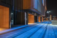 a walkway next to a very tall building at night with bright lights reflecting in the windows