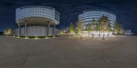 a wide angle of a street at night time with trees in the background, and a circular concrete building