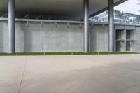 a concrete wall next to some green grass and a building with large columns behind it