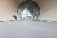 a man stands in an open structure looking at his skateboard in a circular area