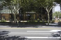 a street scene with two men walking past a burberry store and some trees