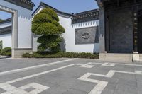 a courtyard at a hotel with white columns and a black doorway with a carved - in figure and a tree with a crown