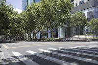 an empty city street next to buildings with trees around it, with two people crossing the cross walk