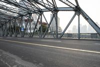 a large long metal bridge with two people on the other side of it and buildings