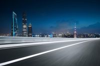 a night shot of the city with skyscrapers and a road going past it with white lines on it