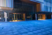 an outdoor area with some large glass doors and a blue tiled floor in front of a tall building at twilight