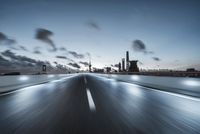 a long way highway at dusk with industrial background and city lights on it, driving to the right