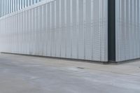 a man riding a red skateboard on a sidewalk next to an industrial building with steel panels on the exterior and side