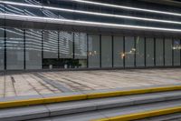 the walkway in front of an outdoor shopping center is shown at night, and its reflective glass windows reflect the lights of the city