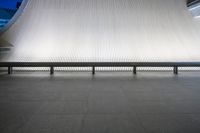 two benches with their legs crossed on the ground next to a large wall that is covered in vertical stripes