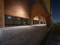 a brick wall with arches leading into a brick building at night near a grass field