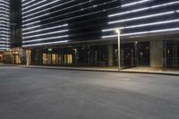 a empty street with lights and a building in the background at night time at the end of a deserted street