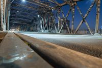 a road going under the metal supports of a bridge over water at night time,