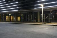 a street with an empty parking lot near a building at night with the lights turned on