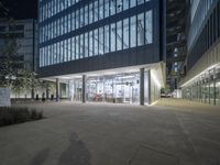 the entrance to a building with windows that are lit up at night and people walking