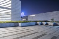 some benches are placed in the middle of an outdoor courtyard with buildings behind them at night