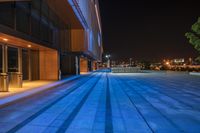 a wide open building with steps to the side of it at night, with city lights in the background