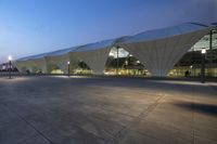 a building with an overhang like structure at night time that appears to be covered by glass and the ground