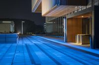 the city's sidewalks are lit by blue lights from buildings on either side of the walkway