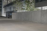 two people walking through an empty parking lot at night time with lights shining on the concrete wall