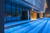 empty sidewalk lit up by lights at night with glass walls and steps in front of building