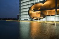 an office building with a lake outside at night in front of it on the waterfront