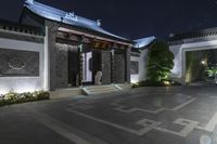 a long entryway is empty at night and features black columns and stone tiles and trees