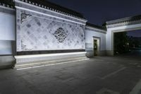 large white wall with decorative stone detailing lit by light at night in dark courtyard area