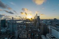 a view of a city, river and tall buildings with the sun coming up over them