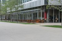 the exterior of a building with tables and benches set against glass walls, along the sidewalk