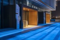 large empty sidewalk next to tall buildings at night, lights on the buildings and floor