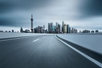 a long asphalt road in front of an urban skyline with buildings behind it on a cloudy day