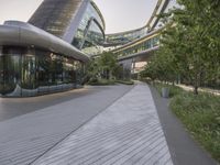 a walkway leading to buildings in an urban area with lots of glass windows and trees in front